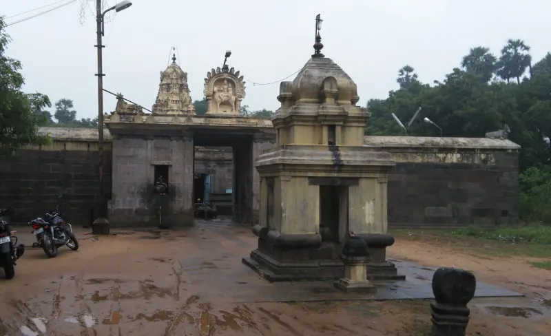 A grey stone gateway topped by two small towers, with a small yellow stone pavilion in front of it.