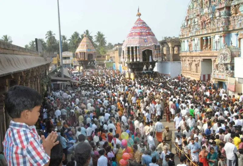 A dense crowd of devotees fills the street, with a temple tower and a domed pavilion behind.