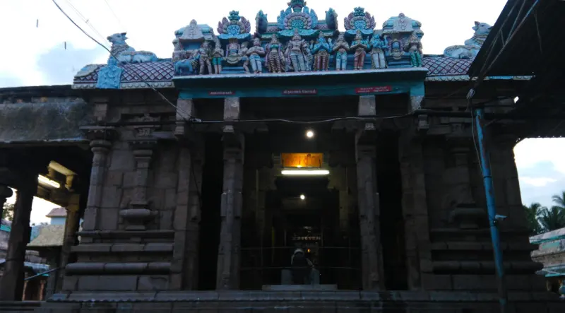 A stone hall with pillars and a lit inner doorway under a roof of coloured sculpted figures.