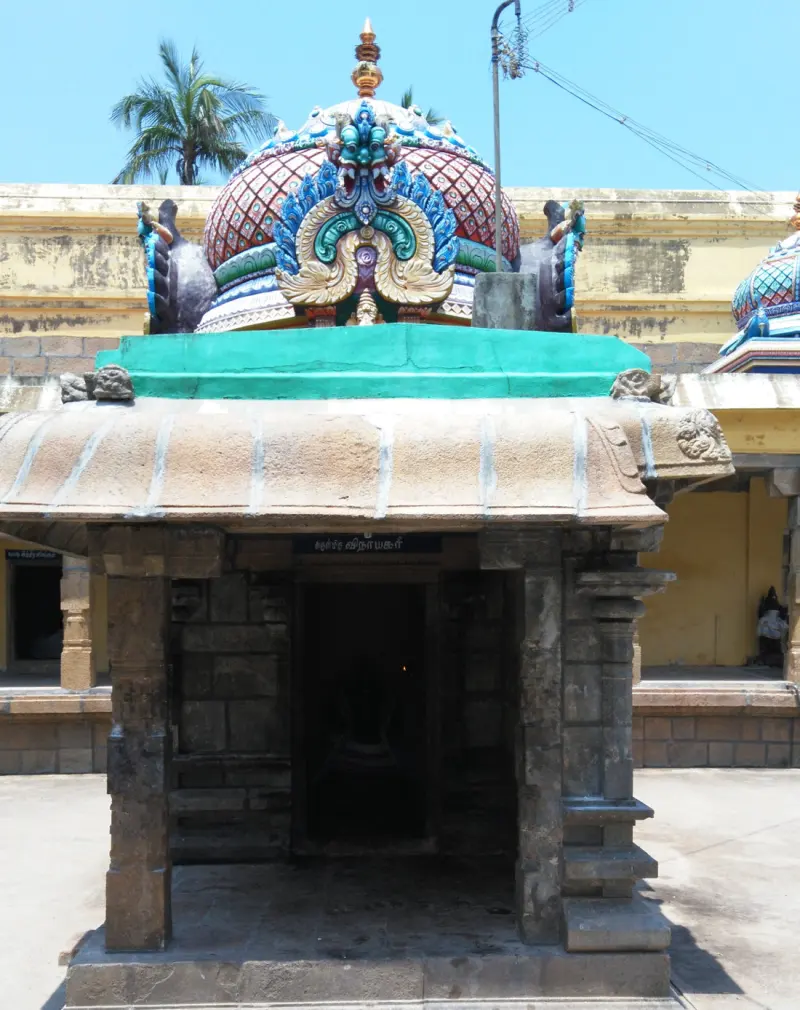 A small stone shrine with a painted dome and a dark doorway, standing in a paved corridor