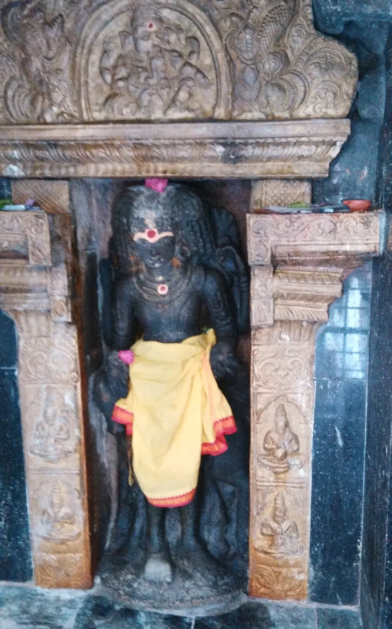 A dark stone figure in a yellow cloth stands in a niche framed by carved pillars and an ornate arch.
