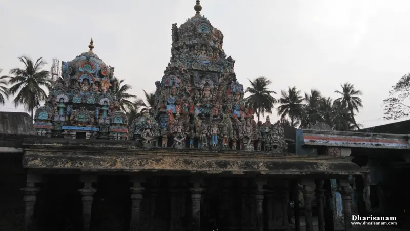 Two colourful towers behind the roof of a stone pillared hall under a pale sky