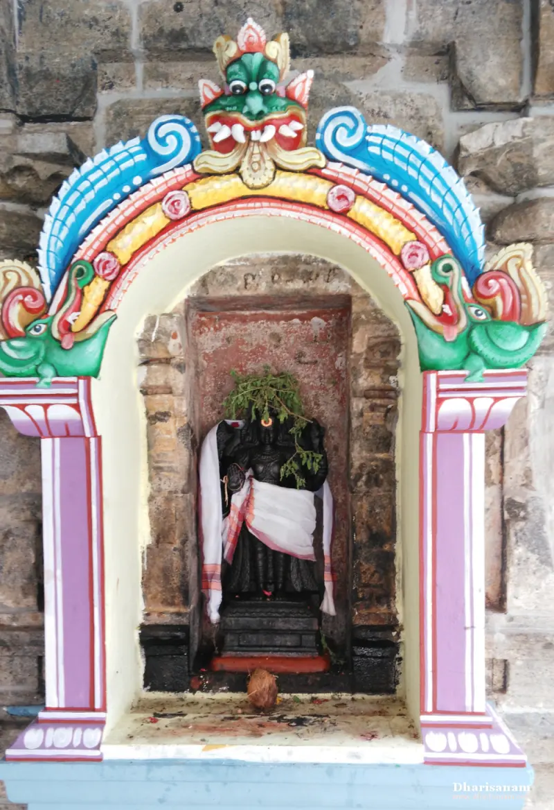 A dark image in white cloth with green leaves on its head, in an arched niche with a painted crest