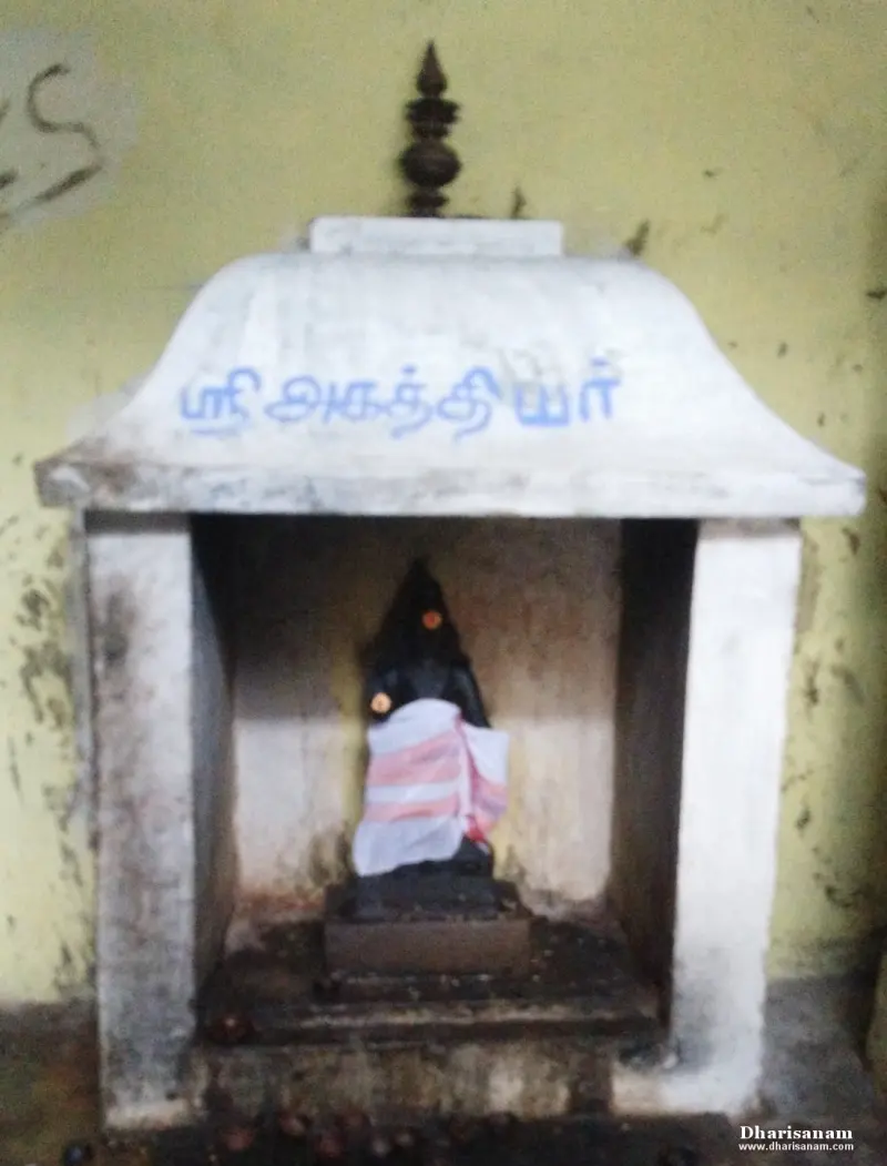 Small white shrine with a Tamil name board above a dark idol draped in cloth
