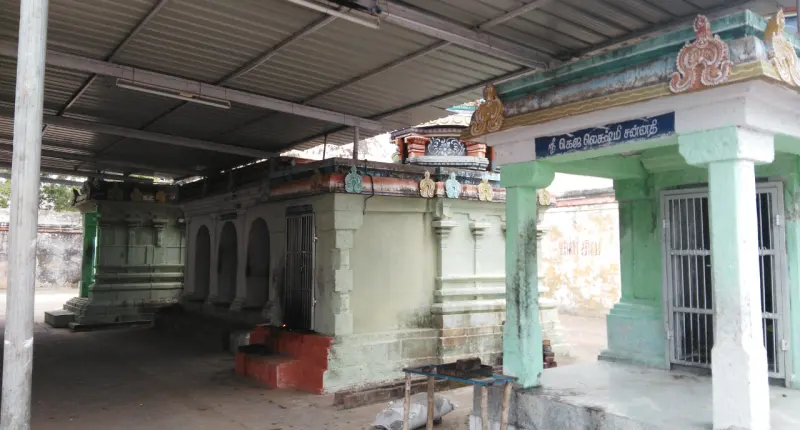 Small shrine buildings under a tin roof, and a green porch with a blue name board on the right.