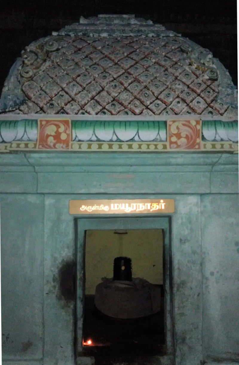 A small shrine with a patterned dome and a lit Tamil sign; a black lingam stands inside the doorway.