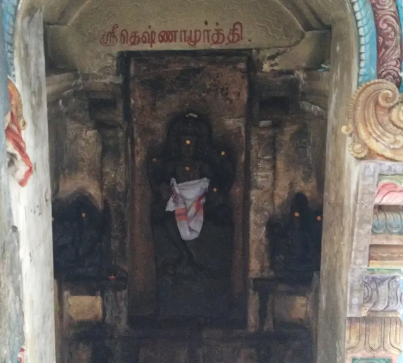 A dark stone idol in a niche, with a Tamil label naming Dakshinamurthi above it