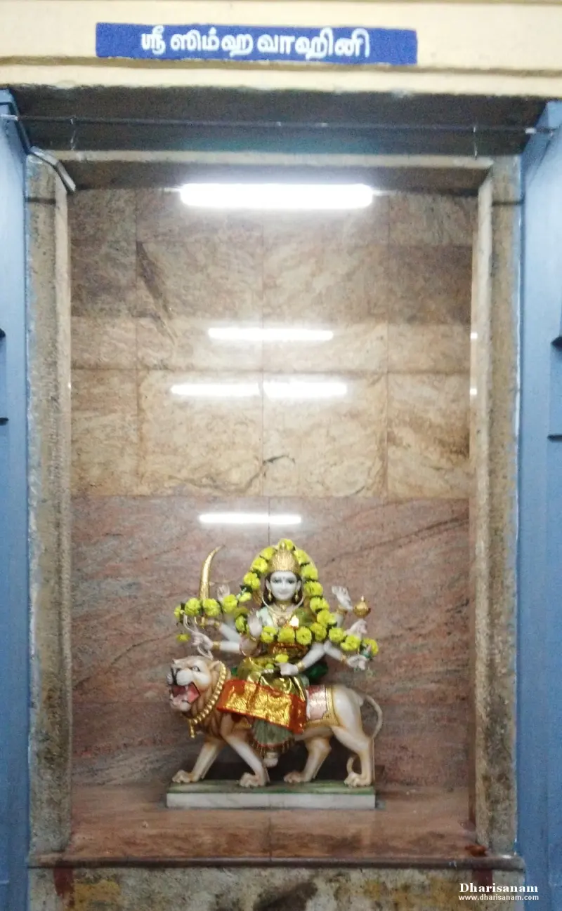 A white marble many-armed goddess seated on a lion, garlanded, inside a tiled niche