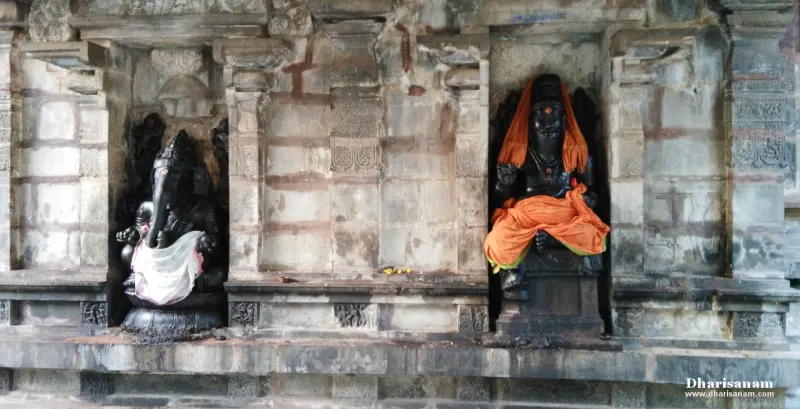 Black stone Vinayakar in white cloth and a seated idol in orange cloth, each in a niche of a stone wall