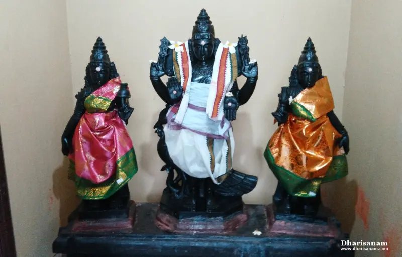 A central black stone idol flanked by two smaller idols in silk, all standing on a low platform