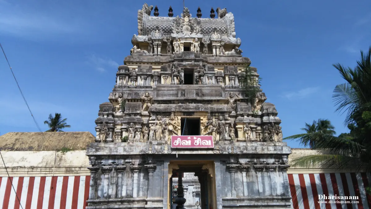 Three-tiered gopuram with carved figures against a blue sky, with a red and white striped wall on either side