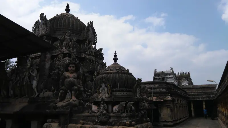 Dark domed shrine towers covered in carved figures, with a gateway tower and a long corridor beyond.