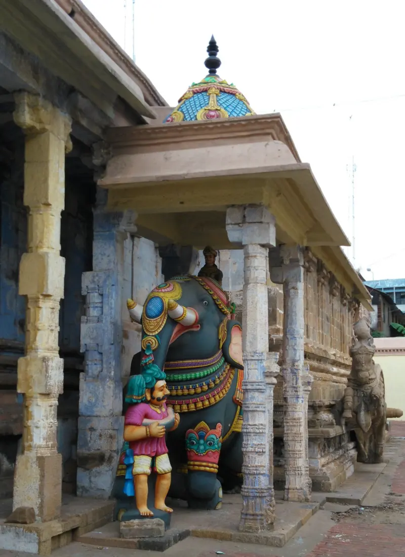 Decorated elephant with keeper between stone pillars, horse beyond