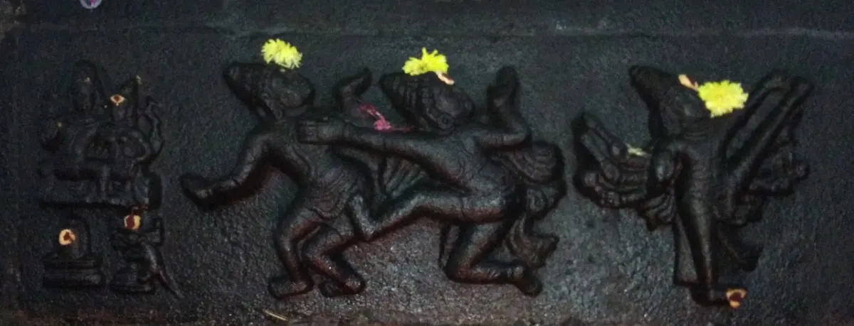 A black stone relief panel with several carved figures in movement, some topped with yellow flowers