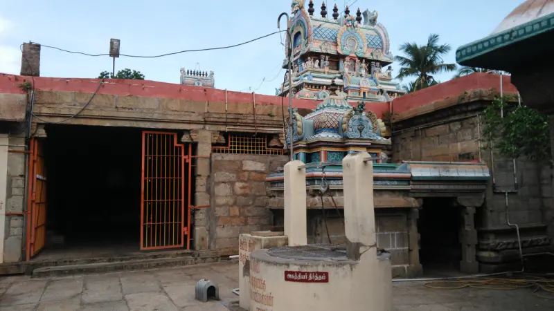 A round stone well with a red name board in front of a corridor, with painted towers behind