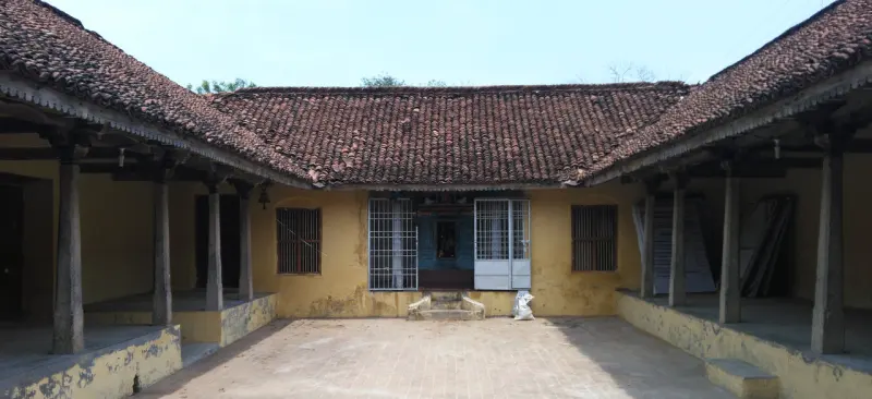 An open courtyard with an old yellow tiled-roof building, a small shrine at its centre