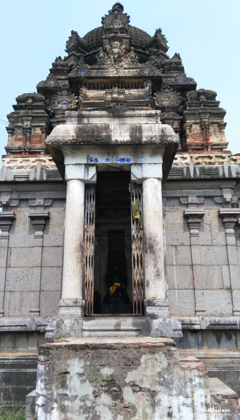 A small stone shrine with two pillars and an open door, under a dark tower with carved figures.