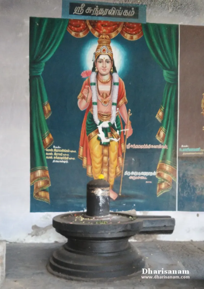 Black stone lingam on a round base in front of a painted figure with a Tamil name board above