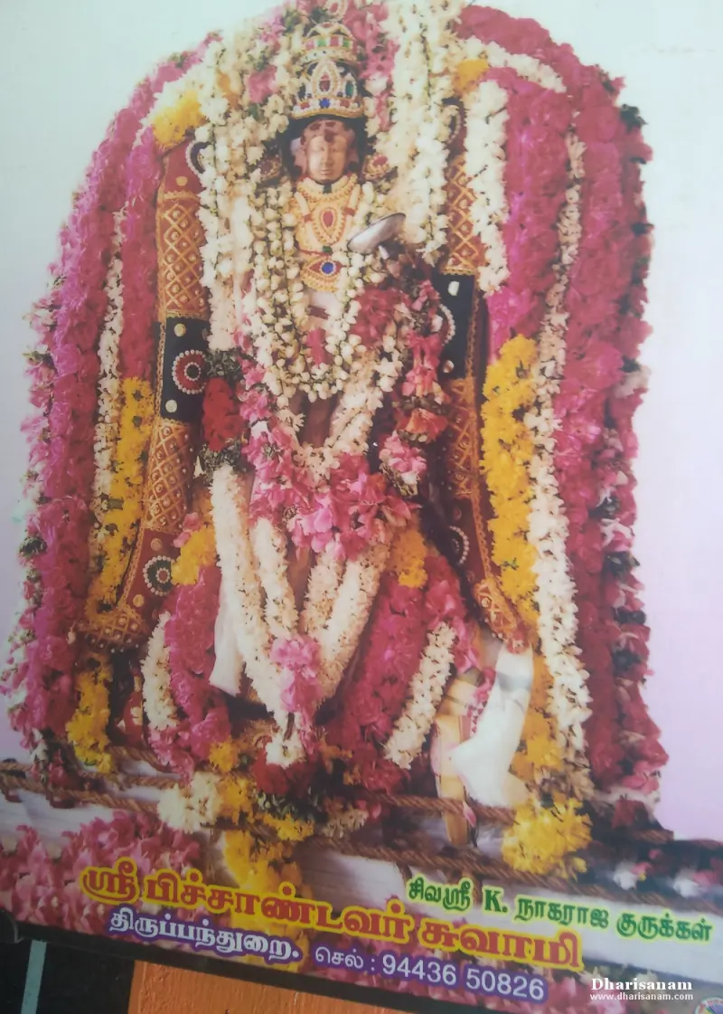 A framed photo of an idol covered in pink, white and yellow garlands, with a Tamil name caption.