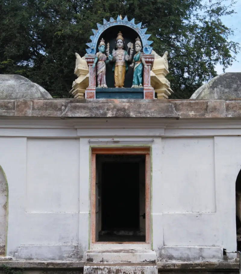 A white corridor shrine with three painted figures set on the roof above a dark doorway