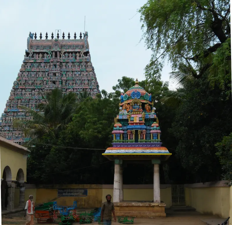Unfinished grey tower behind a small colourful shrine