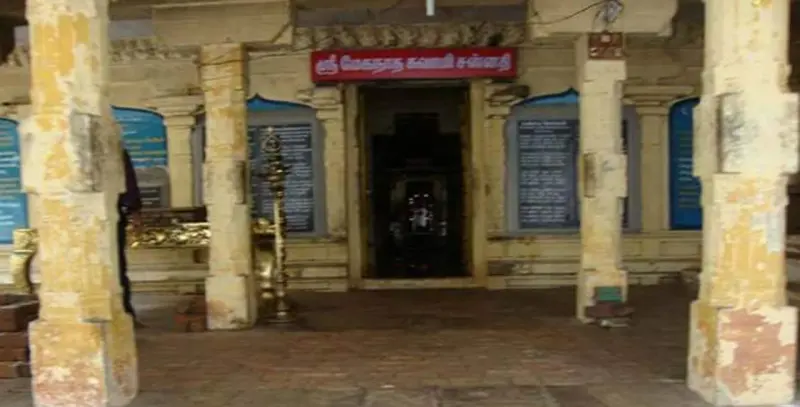 Doorway of the sanctum with a red Tamil name board, a brass lamp and blue notice boards between worn yellow pillars