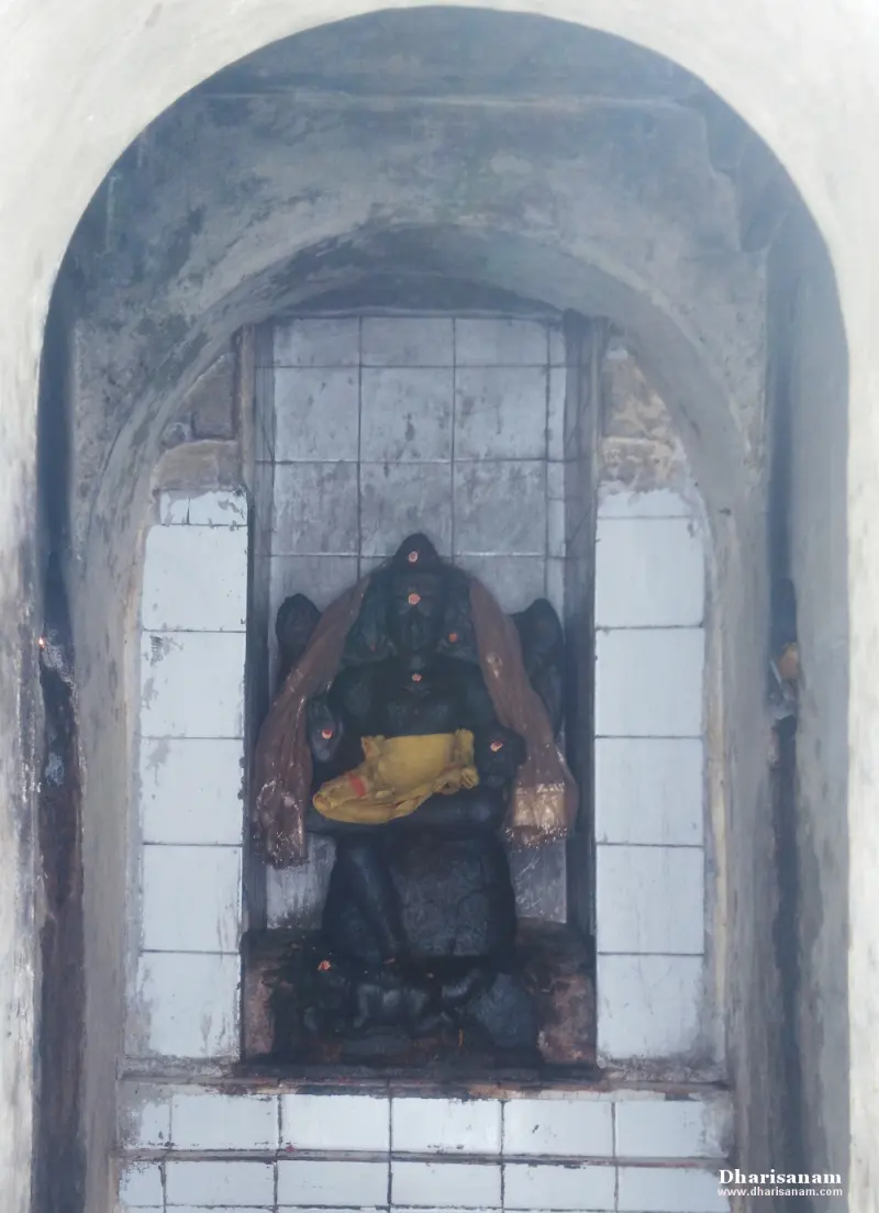 A black stone Vinayakar with a yellow cloth on his lap, seated in an arched niche lined with white tiles