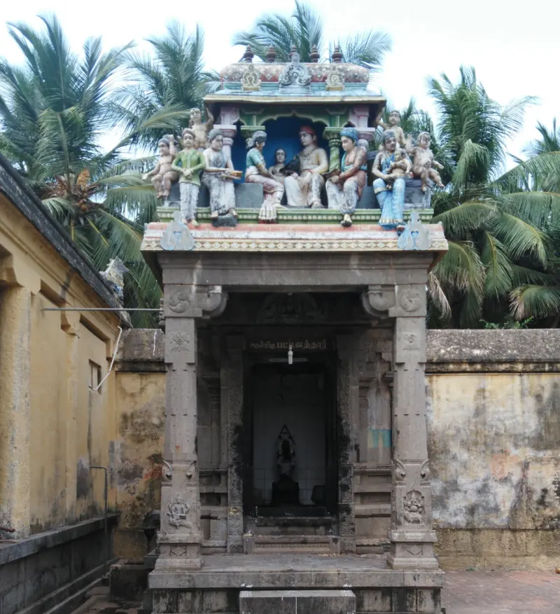 A stone shrine in front of a yellow wall, with painted figures above and palm trees behind