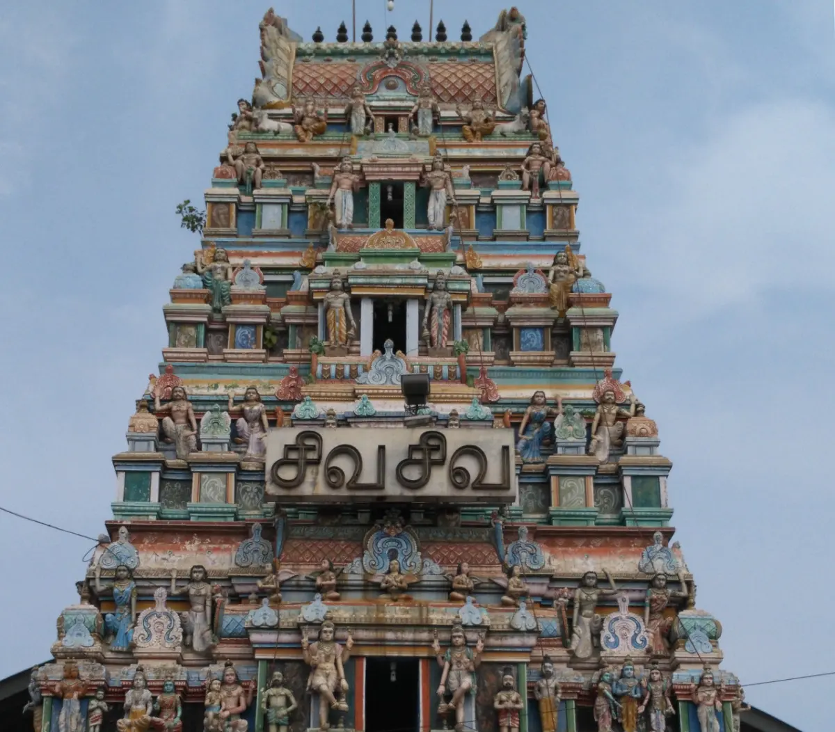Close view of a tiered gopuram with painted figures and a Tamil name board reading Siva Siva.