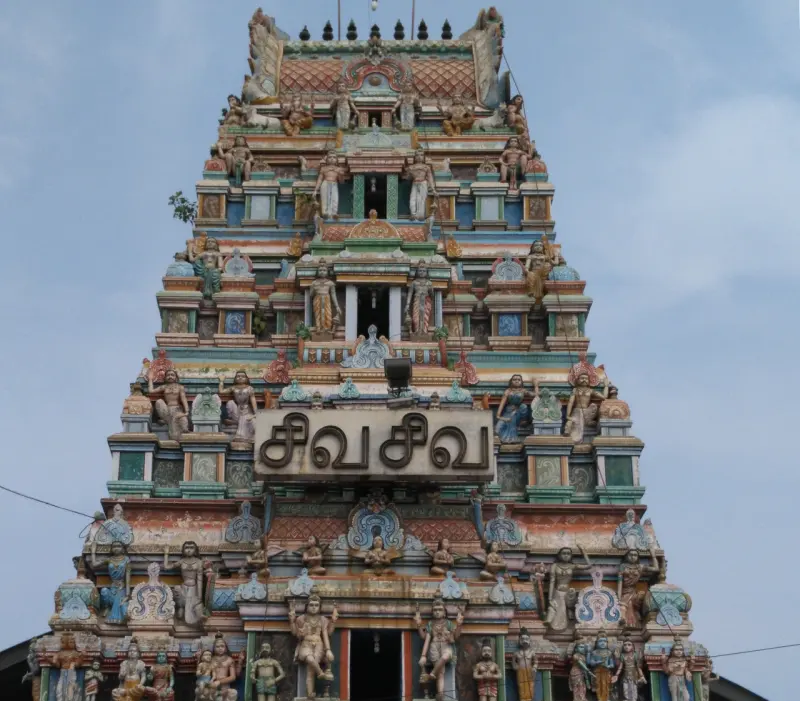 Close view of a tiered gopuram with painted figures and a Tamil name board reading Siva Siva.