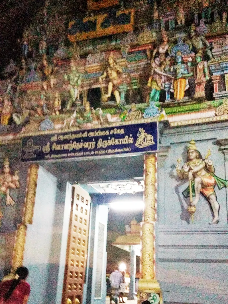 A gateway under a tower of coloured figures, with a blue name board in Tamil above the door