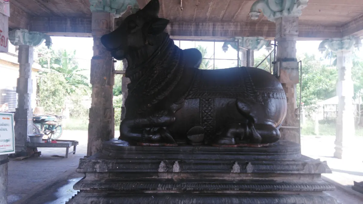 A large dark stone bull seated on a platform under a pillared roof