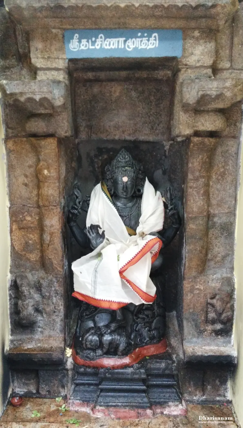 A seated black stone Dakshinamurthy in a niche, in white cloth, with a Tamil name board above