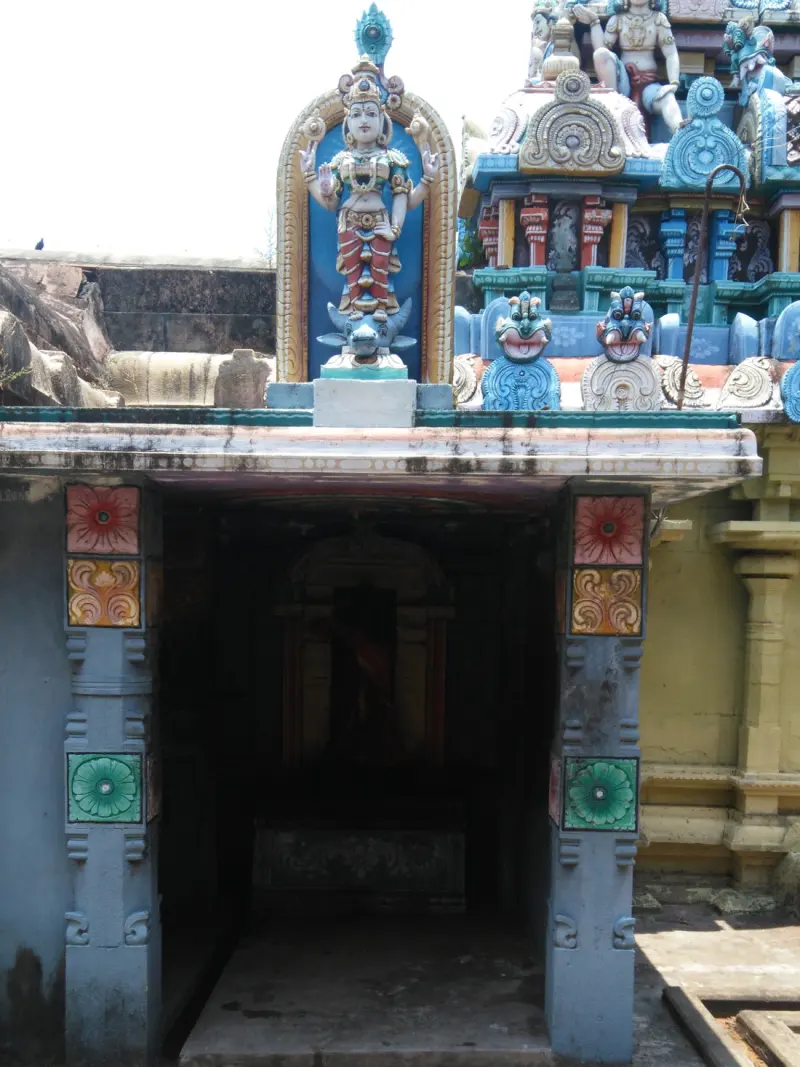 A shrine doorway with a painted standing figure on a bull above it, and a colourful tower beside it.