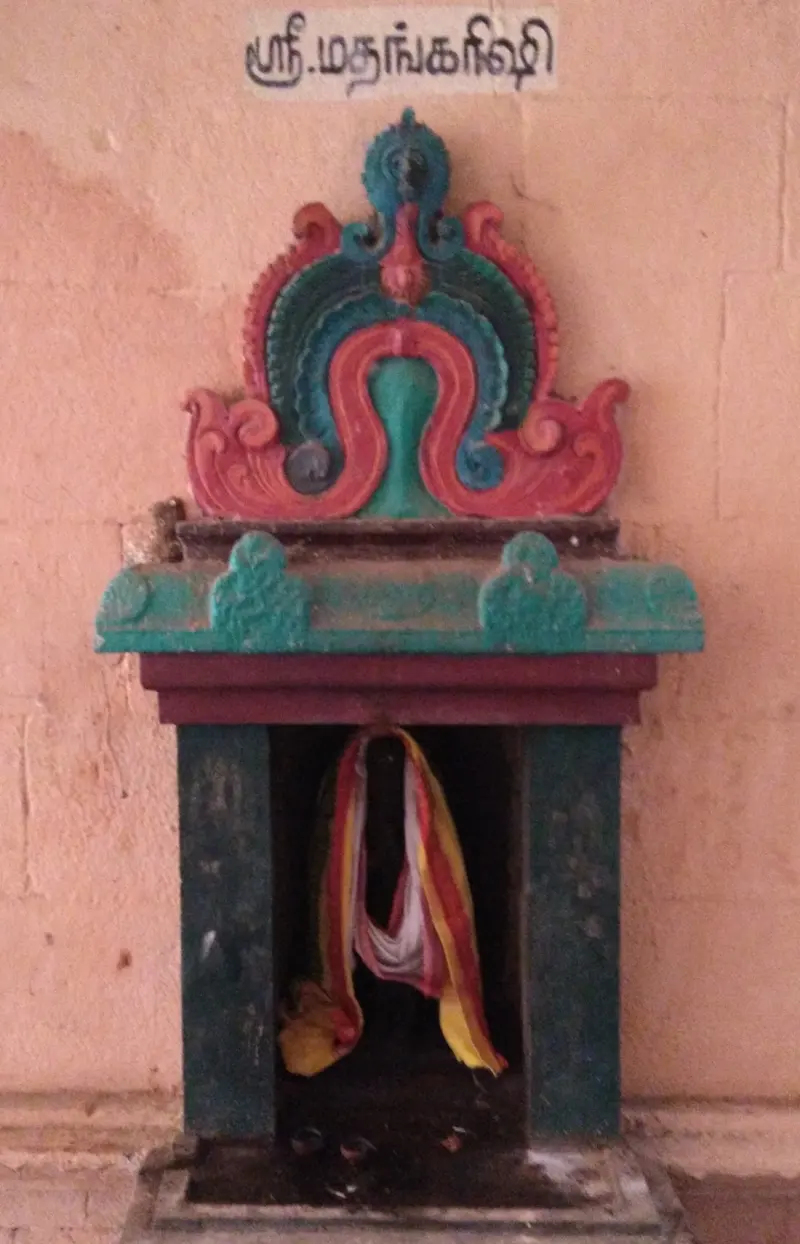 A small painted niche shrine under a Tamil name board, with cloth hanging in the opening.