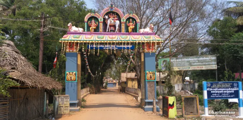 A painted arch with Ganesha and Nandi figures over a village road, with a signboard at the right