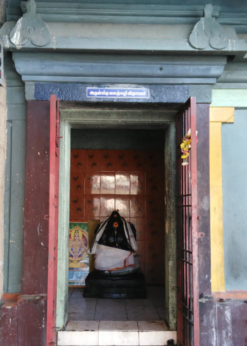 Small shrine with open doors and a black Vinayakar idol dressed in white cloth