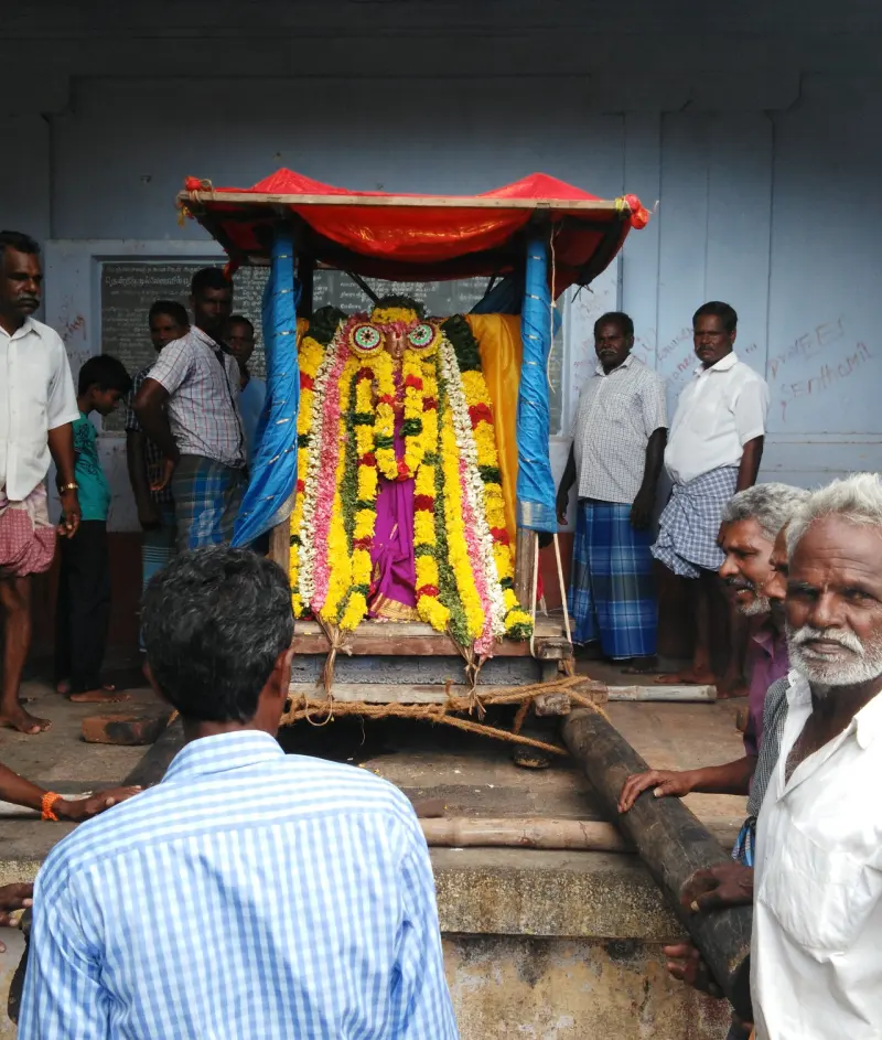 A flower-garlanded idol on a wooden carrier under a red canopy, with men gathered round