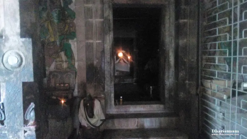 A dim stone doorway with a lit lamp inside and a small cloth-draped Nandi figure beside the steps