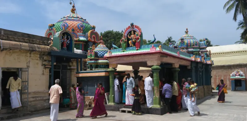 Two colourful shrine roofs with figures on them, devotees standing before them under a blue sky