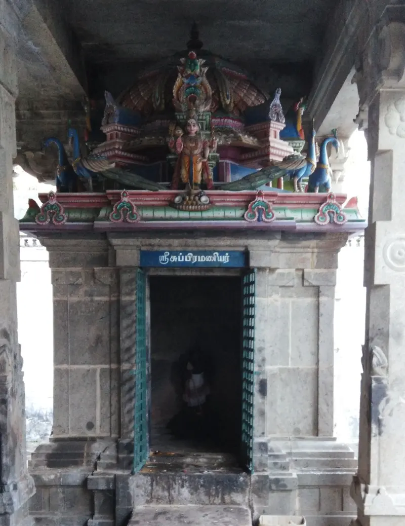 Small stone shrine with a painted peacock roof and a blue Tamil name board