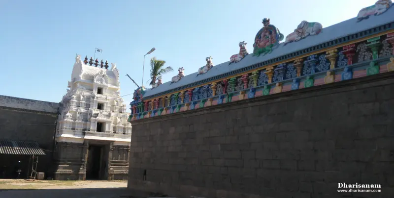A white tower at the left and a long stone wall topped with painted figures at the right.