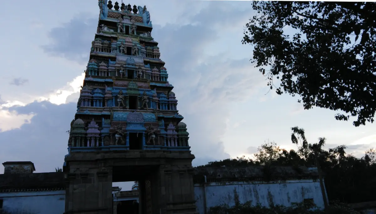 Multi-tiered painted gopuram at dusk, with a white wall and a tree beside it