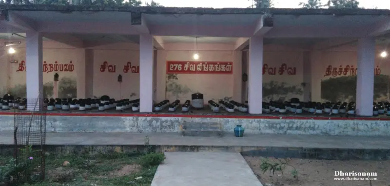 A long open corridor with rows of black lingams and a red board reading 276 Shiva lingams in Tamil.