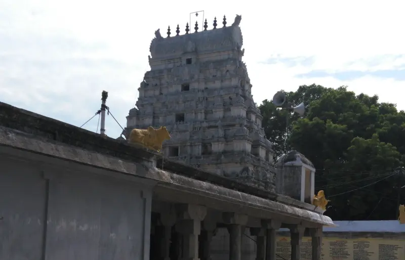 A grey stone gateway tower rising over a corridor roof, with a golden bull statue in front and loudspeakers.
