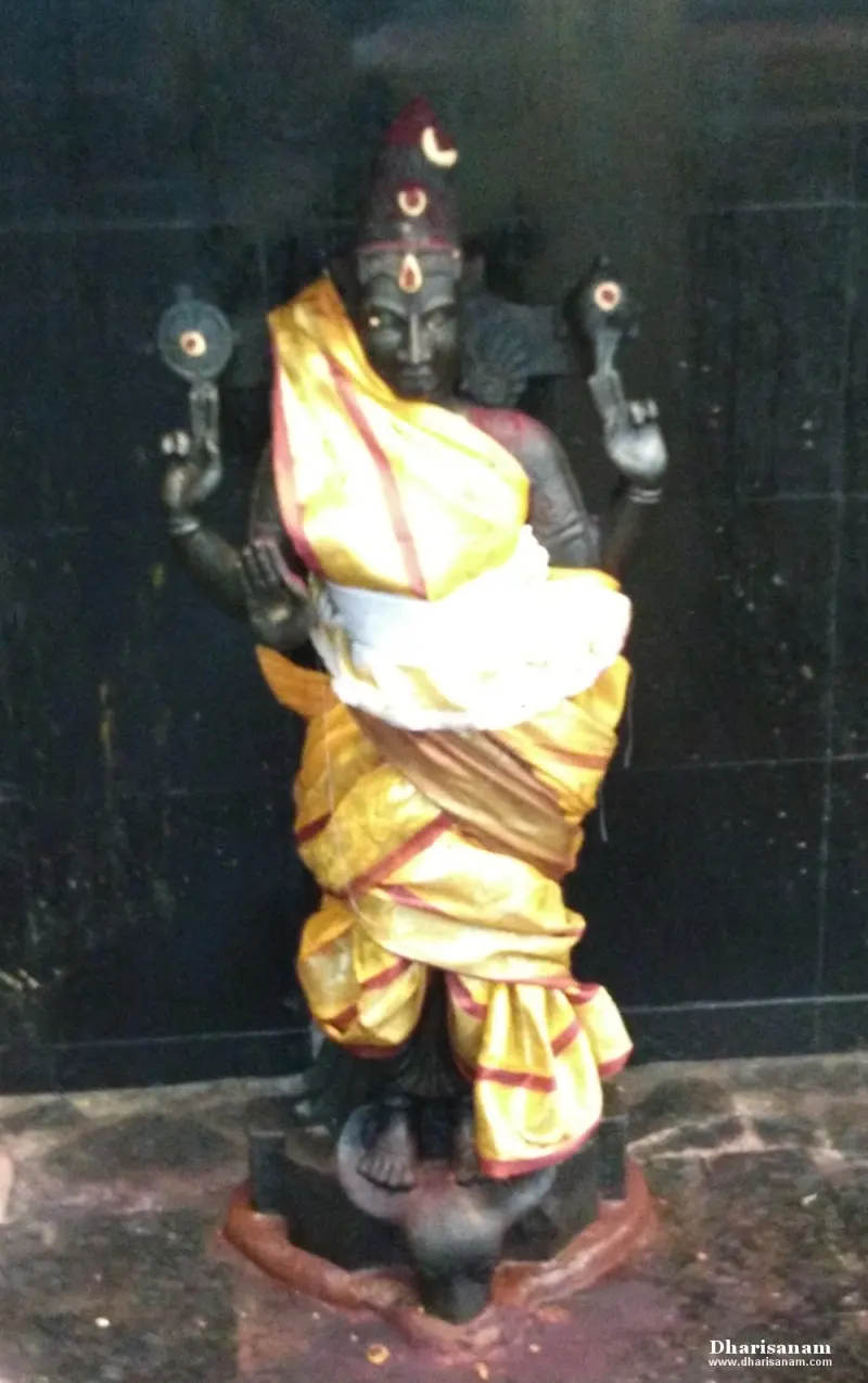 A dark idol with four arms in a yellow and red cloth, two raised hands holding round discs
