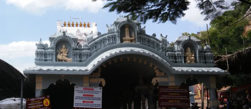 A pale blue and grey gateway with figures of deities in niches above an arched entrance, a hill behind.