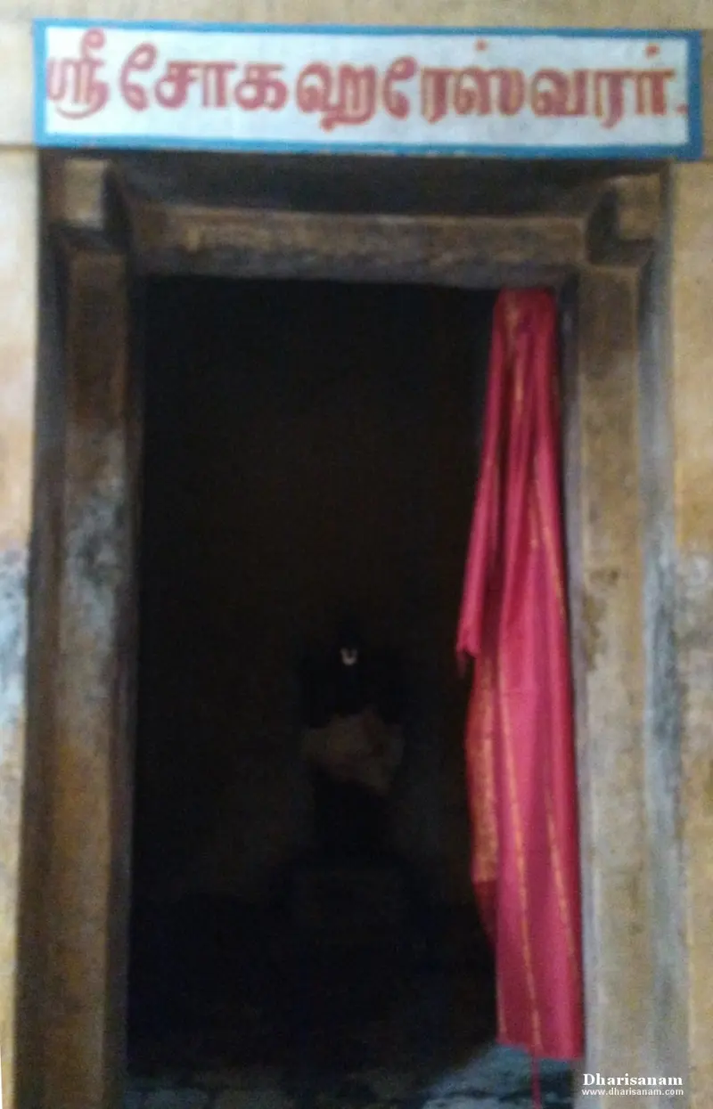 A dark shrine doorway under a Tamil name board, with a red cloth hanging at its side