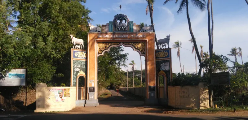 A tall arch gateway with bull figures on top stands on the road, with palm trees behind