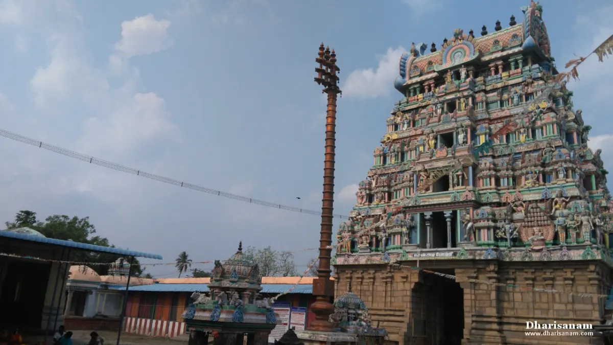 A tall tower covered in painted figures beside a tall flagstaff in the temple courtyard, with small shrines below